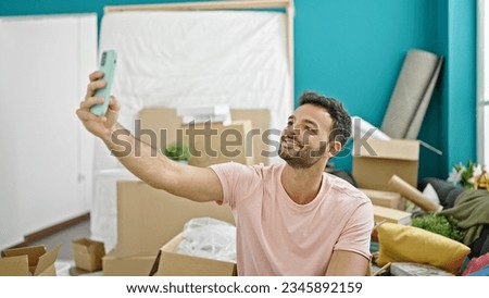 Young hispanic man make selfie by smartphone sitting on sofa at new home