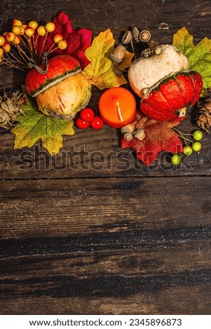 Autumn festive composition on old wooden background. Decorative pumpkin, fall leaves, berries and acorns. Hard light, dark shadow, flat lay, top view