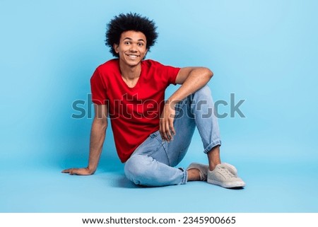 Full length photo of satisfied pleasant positive person wear red t-shirt jeans pants sitting on floor isolated on blue color background