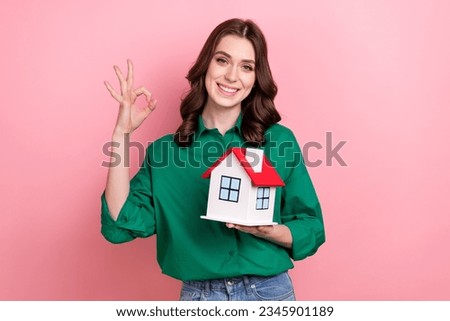 Photo of positive cute lady wear green shirt showing okey holding little house isolated pink color background