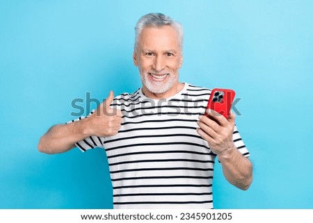 Photo portrait of funny old male showing thumb up hold telephone dressed stylish striped garment isolated on blue color background