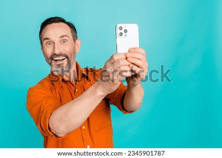 Photo of astonished funny impressed handsome man with gray white beard making photo on smartphone isolated on teal color background