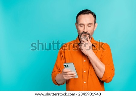 Portrait of ponder pensive man dressed orange shirt look at smartphone read post arm on chin isolated on turquoise color background Royalty-Free Stock Photo #2345901943