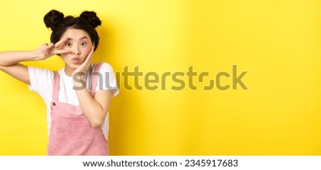 Kawaii asian girl showing v-sign and pouting cute, making silly face with makeup, standing on yellow background.