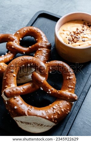Salted pretzels with chilli jalapeño cheese sauce for dipping. Pretzels are large bread type on a dark black and charcoal background. 