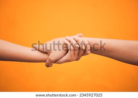 Holding hands, studio and closeup for support, help and care for teamwork by orange background. People, friends and together for solidarity, link and connection with synergy, partnership and strong Royalty-Free Stock Photo #2345927025