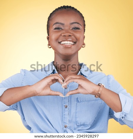Happy black woman, portrait and heart hands for love, care or support against a yellow studio background. Face of African female person smile with loving emoji, shape or symbol icon on valentines day