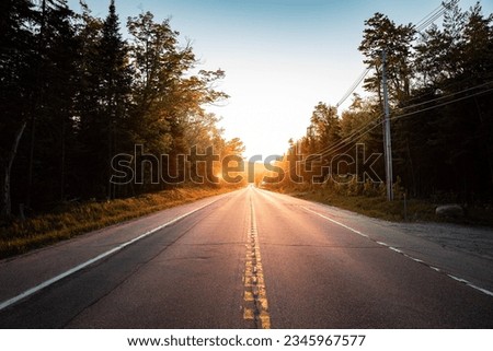 sunset in the mountains with houses close to the river, layers of the mountains, solitary road with the bright sun in the background Royalty-Free Stock Photo #2345967577