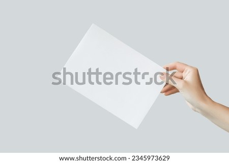 female hand holding blank white a5 poster isolated on gray background
