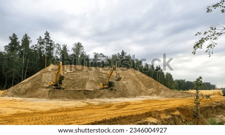 a crawler excavator loads crushed stone and sand into a truck. Large hills and piles of sand, gravel, crushed stone yellow, gray and black.                   