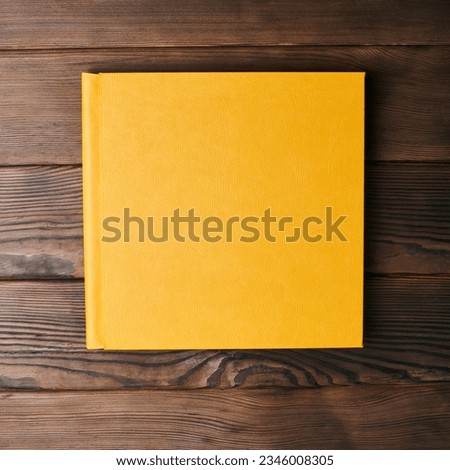Yellow leather hardcover photobook isolated on a wooden background with copy space. Top view, flat lay. Сlosed book binding mockup for adding personalized text or images.