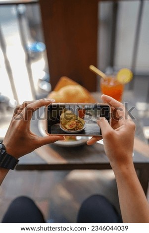 Top view of a young woman taking an aesthetic photo of food using her smartphone in a restaurant