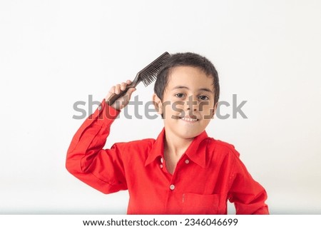 cute boy making a sly face.
A cute looking boy in a red shirt making a slimy face, combing his hair
Studio portrait, concept health with white background.  
funny face.