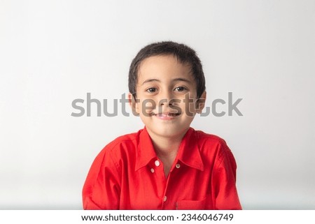 
cute boy making a sly face.
A cute looking boy in a red shirt making a slimy face in white room.
Studio portrait, concept health with white background.  
funny face.
