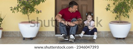 Image of a young father with his daughter smiling, sitting in the doorway while talking and having fun. Homecoming of a family. Horizontal banner 
