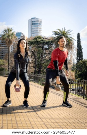Man and woman exercising with dumbbells during a workout in the park.