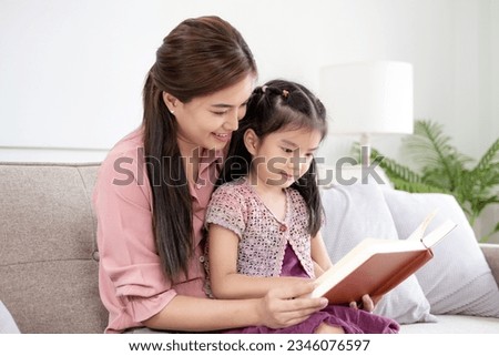Happy asian young mother smile reading fairy tale story with daughter in living room at home. Little girl enjoy with fairy tale story from mom on couch looking book together.Relaxed time at home Royalty-Free Stock Photo #2346076597