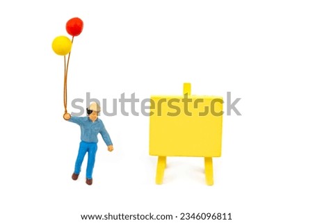selective focus of miniature happy man holding balloon in his hand with yellow sign isolated on white.