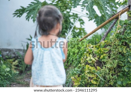A young girl sprays water on the plants with a hose.