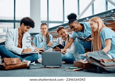 Happy African American medical student and his friends cooperating while e-learning on laptop in lecture hall.  Royalty-Free Stock Photo #2346164343