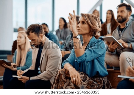 Female entrepreneur raising her hand to answer a question during business conference in convention center.  Royalty-Free Stock Photo #2346168353
