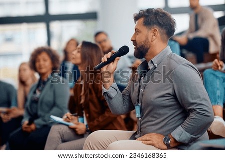 Male entrepreneur asking a question while attending business seminar in conference hall. Royalty-Free Stock Photo #2346168365