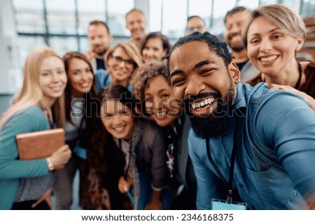 Multiracial group of cheerful business seminar attendees taking selfie in conference hall and looking at camera. 