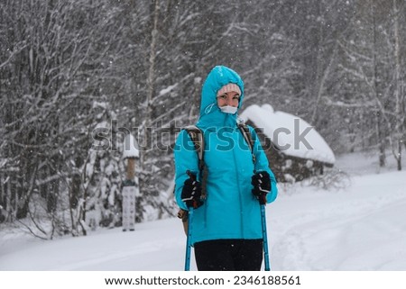 portrait of a sweet hiker girl with a snowy hood on her head; girl walking through a magical snowy forest in the mountains	