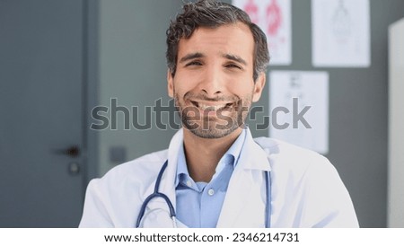 male nurse with stethoscope standing at clinic. He is smiling and looking at the camera.