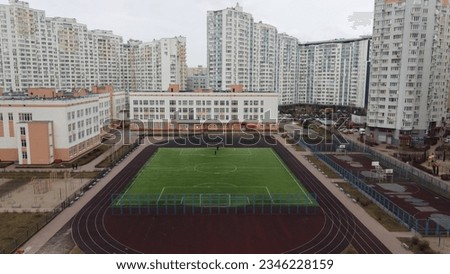 The photo captures a stadium nestled amidst a cluster of high-rise buildings.The football field takes center stage,encircled by a running track,creating a dynamic sports hub within the urban landscape