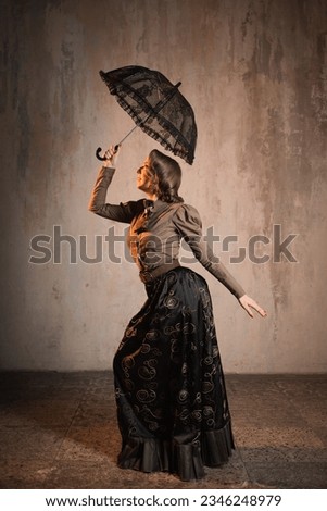 A stylish lady in an elegant Victorian-style suit, in a hat with an umbrella in her hands, is ready to take off like Mary Poppins Royalty-Free Stock Photo #2346248979