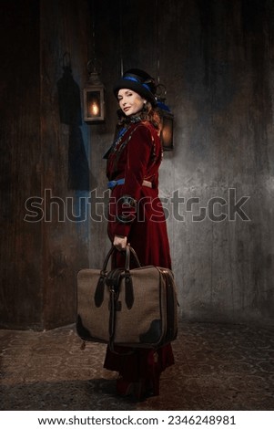 A stylish lady in a burgundy old-fashioned suit with a hat and a valise. Brunette in a retro style suit Royalty-Free Stock Photo #2346248981