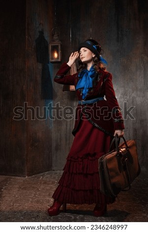 A stylish lady in a burgundy old-fashioned suit with a hat and a valise. Brunette in a retro style suit Royalty-Free Stock Photo #2346248997