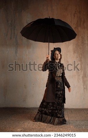 A stylish lady in an elegant Victorian-style suit, in a hat with an umbrella in her hands, is ready to take off like Mary Poppins Royalty-Free Stock Photo #2346249015