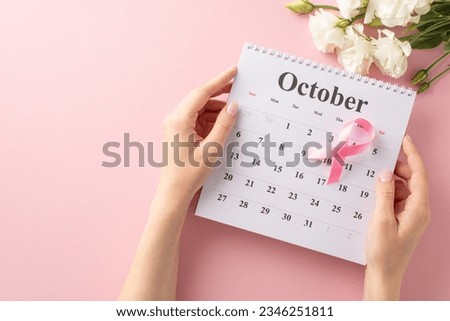 Breast cancer awareness theme. Top view of hands holding calendar displaying October, preparing for medical appointment. Featuring pink ribbon, eustoma flowers on soft pink backdrop with space for ad