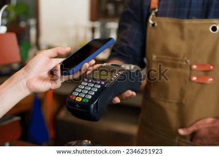 Close-up customer hand is using smartphone to scan QR code from credit card reader to pay for coffee and bakery. Minimize contact and don't use cash to pay. In a cafe while traveling