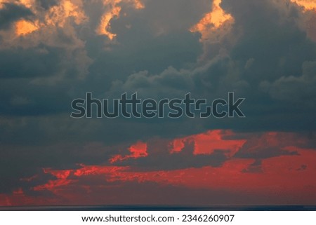 This photo shows a cloudy sunset over a body of water. The sky is ablaze with color, from the deep oranges and reds of the sunset to the wispy white clouds.