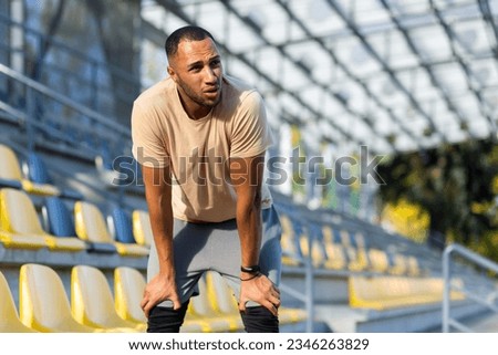Tired hispanic athlete bent over and breathing after jogging, man doing sports on sunny day with active exercises and fitness, athlete resting after jogging. Royalty-Free Stock Photo #2346263829