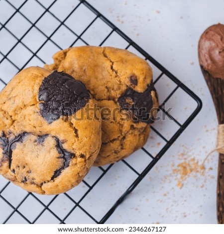 Freshly baked Chunky Chocolate Cookies on cooling rack, nutella, milk on white background