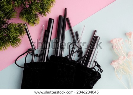 reusable pack of black stainless steel straws and cleaning brush in black cotton bag on pink and blue background, eco friendly lifestyle