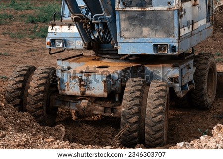 An old rusty blue excavator stands on a construction site. The rusty bucket of an old excavator is lowered to the ground. Royalty-Free Stock Photo #2346303707