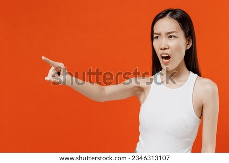 Irritated unnerved aggrieved displeased dissatisfied young woman of Asian ethnicity 20s years old in white tank top point index finger aside scream isolated on plain orange background studio portrait Royalty-Free Stock Photo #2346313107