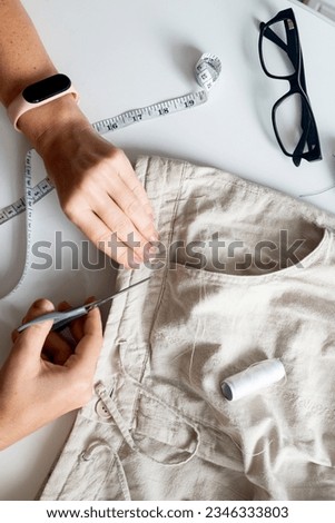 woman seamstress sews linen gray trousers. Sewing and home needlework. Circular fashion, fast fashion, Sustainable, zero waste lifestyle concept Royalty-Free Stock Photo #2346333803