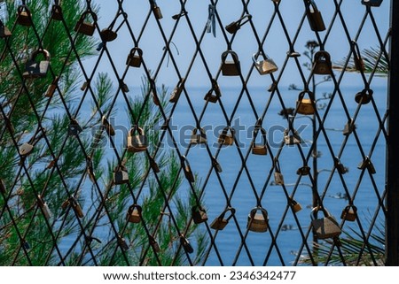 A mesh fence on the seashore with padlocks symbolizing love. Love locks are hung on the fence in large numbers on the sea promenade. Sea on background.