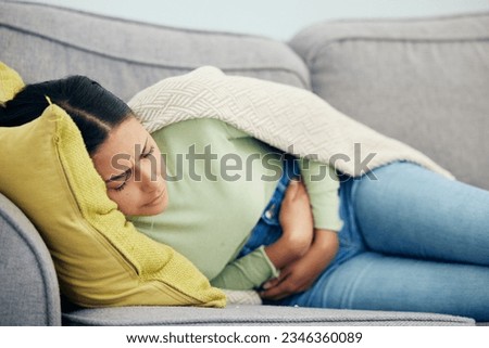 Stomach pain, pms and woman on a sofa with stress, bad or gut health, gas or ibs in her home. Abdomen, anxiety and female person in living room with gas, digestion or constipation from endometriosis Royalty-Free Stock Photo #2346360089