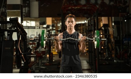 A portrait of a male weightlifter in black sportswear. He does barbell fitness workout in the modern gym.