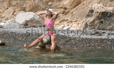 Woman travel sea. Woman traveler captures sea memory in pink bikini, posing on beach amidst volcanic mountains for adventurous journey. Happy tourist enjoys outdoor photography.