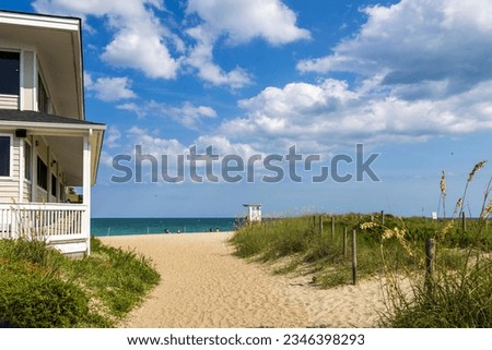 A gorgeous summer landscape at the beach with blue ocean water, silky brown sand, lush green plants and grass, a lifeguard tower, blue sky and clouds in Wrightsville Beach North Carolina USA Royalty-Free Stock Photo #2346398293