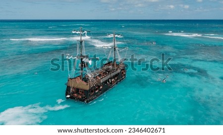 A large thematic pirate ship in the Caribbean Sea on turquoise blue waters. The predominant color of the water is azure. People are swimming near the ship.
