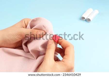 Woman sewing on pink fabric with thimble and needle against light blue background, closeup